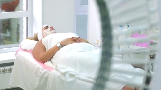 Kobieta kładzie relaks w salonie kosmetologii spa z białą maską na twarzy. — Wideo stockowe