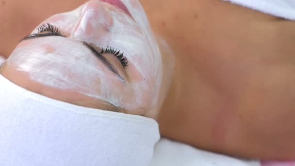 Portrait of woman laying in spa cosmetology salon with white mask on face. — Stockvideo