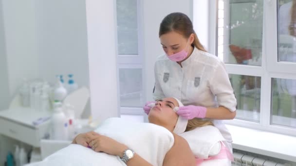 戴手套擦拭年轻客户女性面部面具的美容师. — 图库视频影像