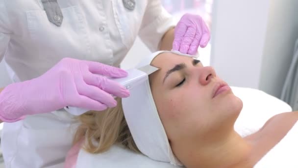 Kosmetolog wykonuje ultradźwiękowy zabieg oczyszczania twarzy młodej kobiecie w klinice. — Wideo stockowe