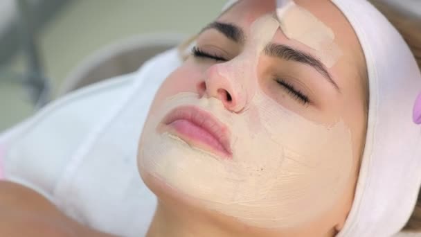 Cosmetólogo aplicando mascarilla para el cuidado de la piel en la cara del cliente mujer en clínica de belleza . — Vídeo de stock