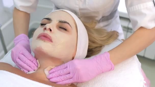 Eldivenli kozmetik uzmanı, kadın yüz ve boynundaki maskeyi siliyor, yakın plan portre.. — Stok video