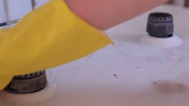 Kadın eli sarı lastik eldivenler mutfakta kirli gaz sobasını yıkar..