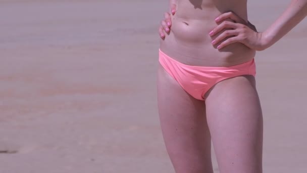 Женщины стройные тело в бикини брюки на пляже с морским песком она стоит солнечная ванна отпуск . — стоковое видео