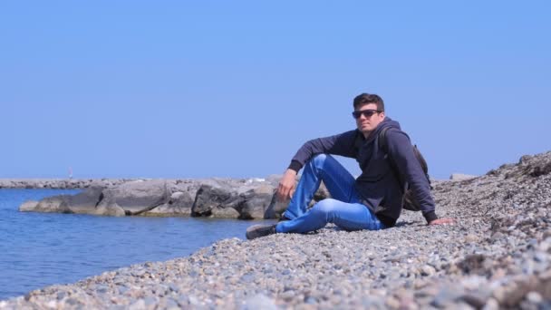 Happy man touriste se trouve à la plage de pierre et regarde la mer en vacances . — Video