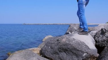 Deniz kıyısına gelen gezgin, tatilde deniz manzarasına hayran olan büyük taşlarda oturur..