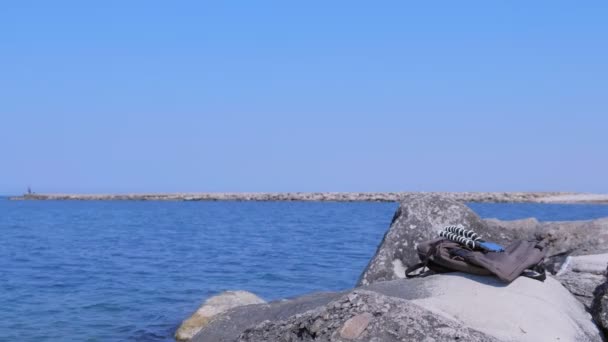 Рюкзак і смартфон на тринозі на величезному камені на морському пляжі . — стокове відео