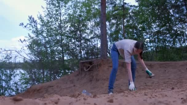 Wolontariuszka zbiera odpady na piaszczystej plaży w pobliżu jeziora, zbiera śmieci w torbie. — Wideo stockowe