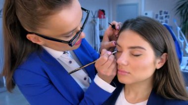 Güzellik salonunda fırça ile kız göz kapakları üzerinde sanatçı boyama okları makyaj.