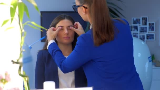 Maquiagem artista aplicando creme tom base nas pálpebras menina esfregando os dedos no salão . — Vídeo de Stock