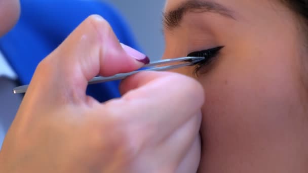 Maquillaje artista pega pestañas artificiales a modelo chica en salón, primer plano de los ojos . — Vídeos de Stock