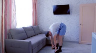 Komik nerd adam evde bacaklar için ileri yamaçlar ve germe egzersizleri yapıyor. Spor mizah konsepti.