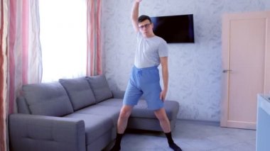 Funny nerd man is doing aerobics exercises at home. Sport humor concept.