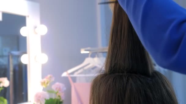 Hair stylist works with long girl hair preparing to cut folding hair into a bun. — Stok video