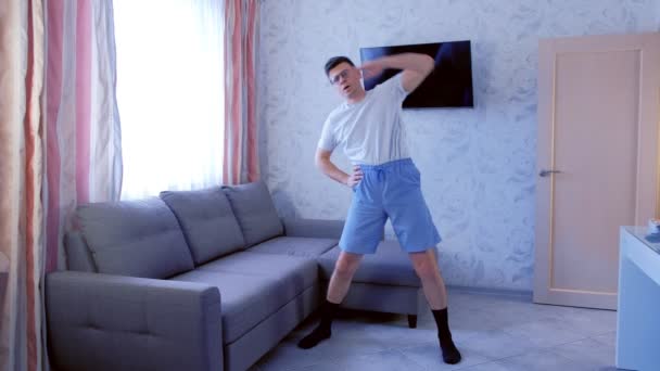 Hombre nerd divertido cansado está haciendo inclinaciones laterales ejercicio en casa en la sala de estar. Limpia el sudor de su frente con su mano . — Vídeos de Stock