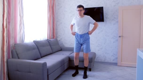 Engraçado nerd homem está fazendo agachamentos exercício em casa na sala de estar. Engraçado puxa para cima shorts antes do exercício . — Vídeo de Stock