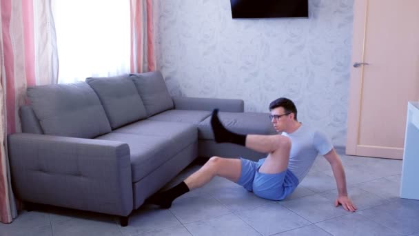 Engraçado nerd homem está fazendo exercícios abdominais levantando as pernas para o peito em casa. Conceito de humor esportivo . — Vídeo de Stock