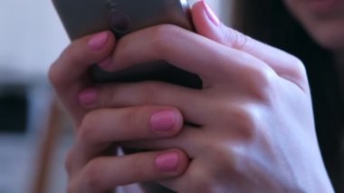 Woman holds smartphone in hands browsing internet types message online surfing.
