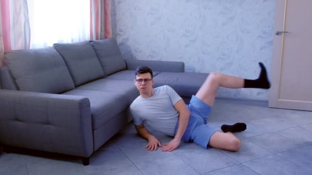 Crazy nerd man doet grappige shaping oefeningen voor benen die thuis op de vloer leggen. Sport humor concept. — Stockvideo