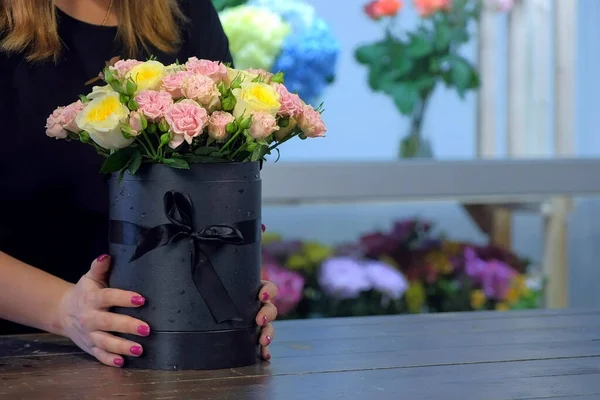 Florist woman putting bouquet of roses at table in floral shop, closeup view.