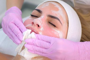 Eldivenli kozmetik uzmanı kadın yüzünden maske siliyor, yakın plan portre..