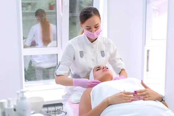 Cosmetologist in handschoenen wast reinigt klanten vrouw gezicht vegen met servetten. — Stockfoto
