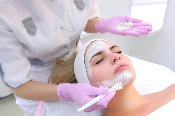 Cosmetologo sta applicando maschera bianca sulla faccia cliente donna in clinica di bellezza . — Foto Stock