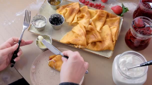 Vrouw eet Russische traditionele pannenkoeken, blini geserveerd met jam, zure room en aardbei op het bord. Close-up bovenaanzicht. — Stockvideo