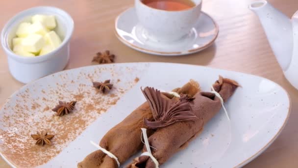 Crêpes russes au chocolat, blinis avec garniture caillée sur l'assiette. Servi avec une tasse de thé et de beurre. Vue latérale . — Video