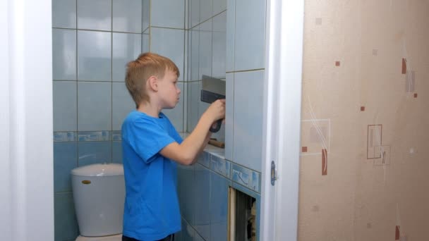 Chłopiec przeprowadza remont, usuwa płytki ze ściany w toalecie za pomocą szpachelki. — Wideo stockowe