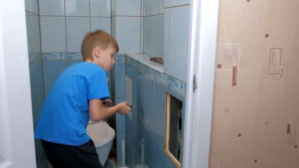 Child boy makes renovation repair at home, he removes tiles from wall in toilet. — Stock Video