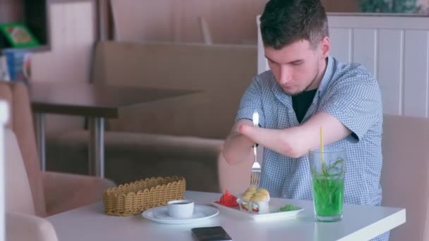 Un homme handicapé avec deux mains amputées mange des rouleaux de sushi dans un café avec une fourchette . — Video