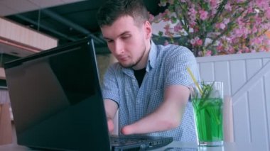 Kafede iki kütük eli ampütlü engelli genç adam dizüstü bilgisayarda çalışıyor.