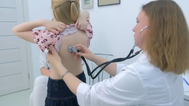 Mujer pediatra escuchando el latido del corazón de una niña usando estetoscopio en la clínica . — Vídeo de stock