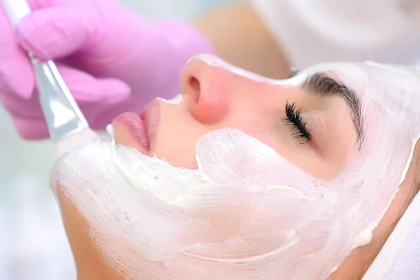 Cosmetologo sta applicando maschera bianca sulla faccia cliente donna in clinica di bellezza . — Foto Stock