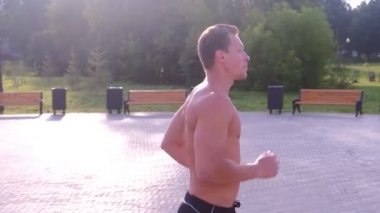 Genç sporcu şehir parkında çıplak gövdesiyle koşuyor..