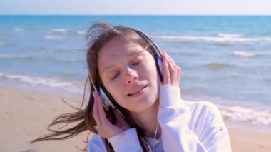 Kulaklıklı genç kadının portresi deniz kumu plajında müzik yürüyüşlerinin keyfini çıkarıyor.