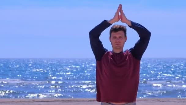 Young man is meditating on the sea beach making hands in namaste pose. — 비디오