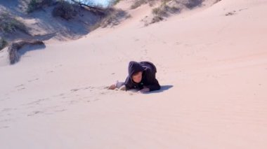 Mutlu çocuk tatilde kumsaldaki kum tepeciğine tırmanıyor..