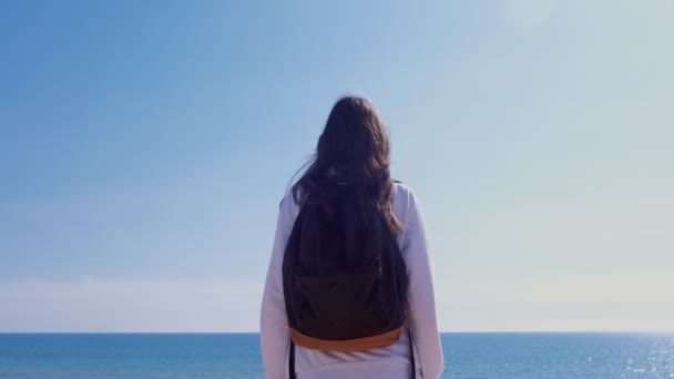 Fille voyageur avec sac à dos stands regarde la mer sur les vacances vue de côté extérieur . — Video