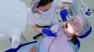 Diş hekimi ultrason temizliği sırasında tükürük ejektör kullanımı kadın dişleri üzerine su dökün.