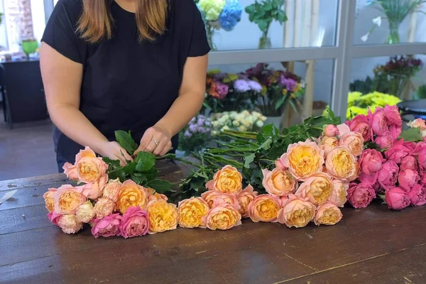 Florist woman making bouquet of pink peonies in flower shop, closeup view.