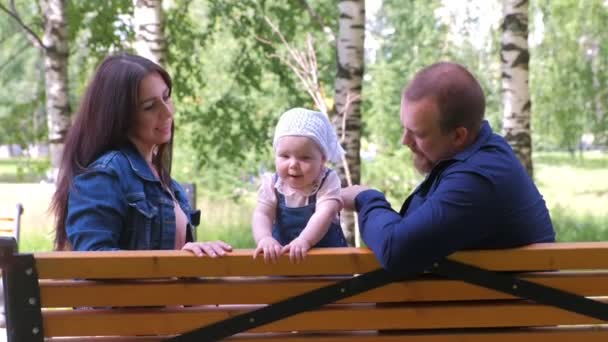 Сімейна мама і тато сидять і грають на лавці в міському парку з маленькою дівчинкою . — стокове відео