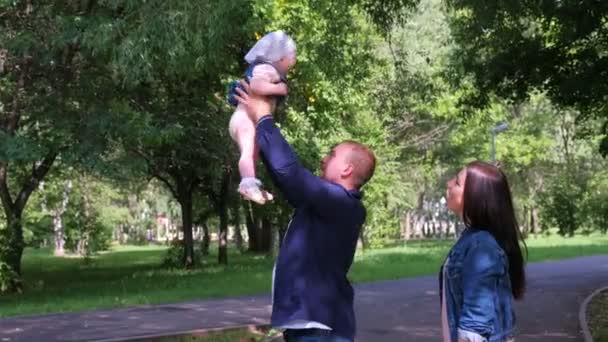 Pappa kastar sin dotter i luften och fångar i stadsparken, mamma står nära familjen. — Stockvideo