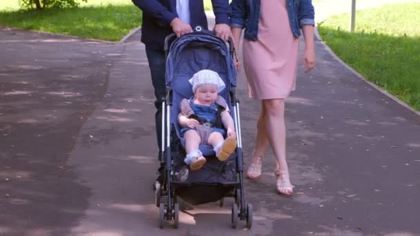 坐在婴儿车里的女婴与父母一起在城市公园里散步，近距离观看. — 图库视频影像