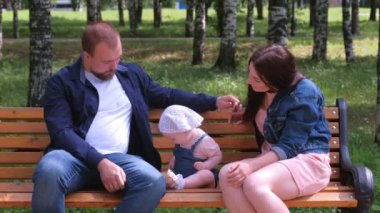 Aile portresi anne, baba şehir parkında bankta oturmuş bebekle konuşuyor..