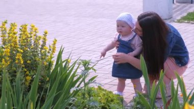 Anne kızıyla parkta yürüyor, onu tutuyor ve çiçeklere bakıyor..
