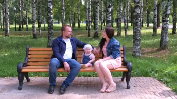 Familie portret moeder, vader zitten praten op bank in stadspark met baby meisje. — Stockvideo
