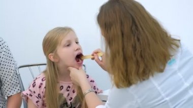 Pediyatrist kadın spatula ve fener kullanarak boğaz ağrısı çeken kız çocuğu arıyor..