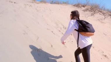 Girl tourist climbs up on high sand dune at seashore outdoor hiking on vacation.